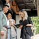 Smiling Real Estate Agent Showing Documents To Interracial Couple With Paper Cup Near Cottage